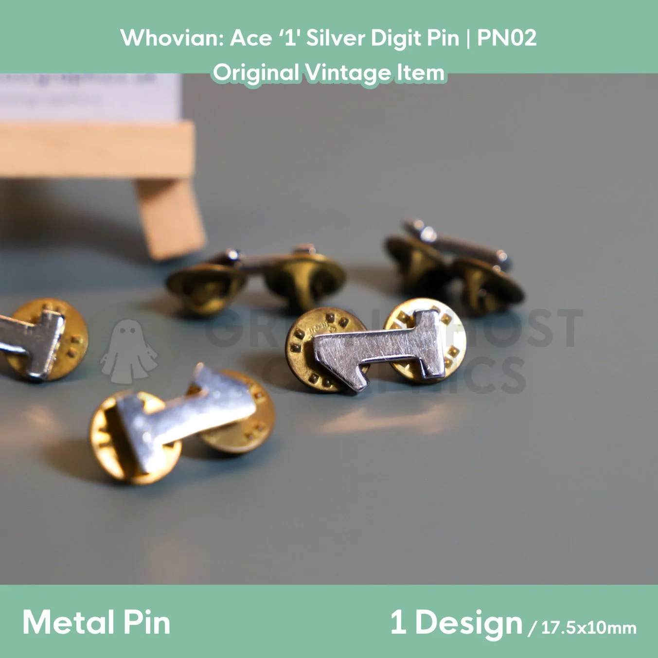 Several silver number “1” metal pins with gold butterfly clasps arranged on a tabletop beneath a display stand.