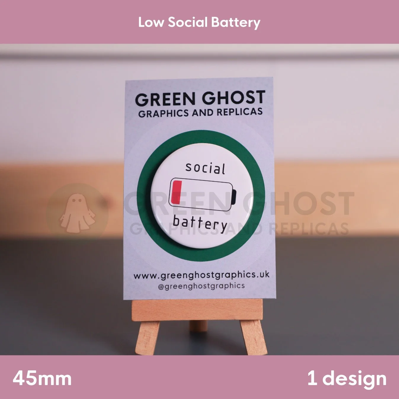 A circular white badge showing a low‑battery symbol with “social battery” mounted on a branded card on a wooden easel.