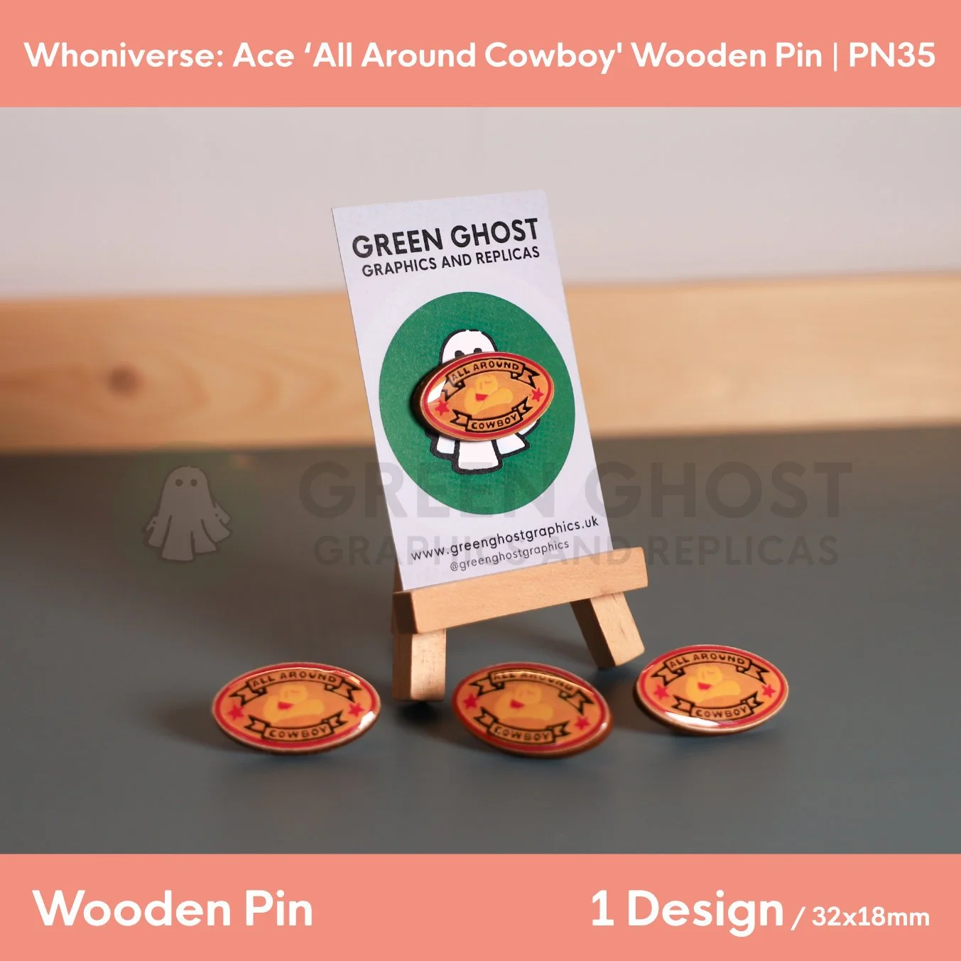 An oval “ALL AROUND COWBOY” wooden pin attached to a branded backing card on a wooden easel, with several identical pins scattered around the base.