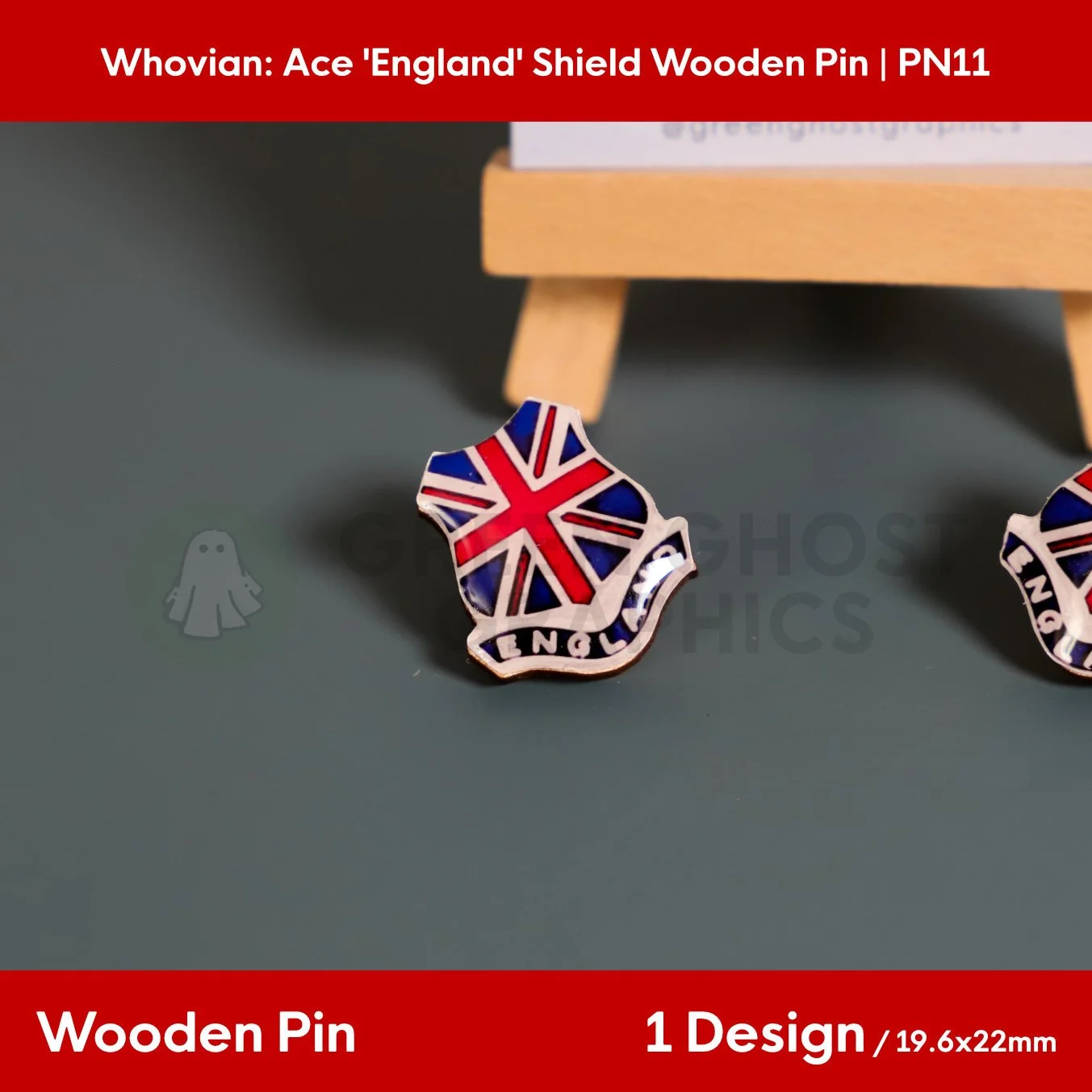 A shield‑shaped wooden pin with a red, white, and blue Union Jack design and the text “ENGLAND” displayed on a flat surface beside a wooden easel.