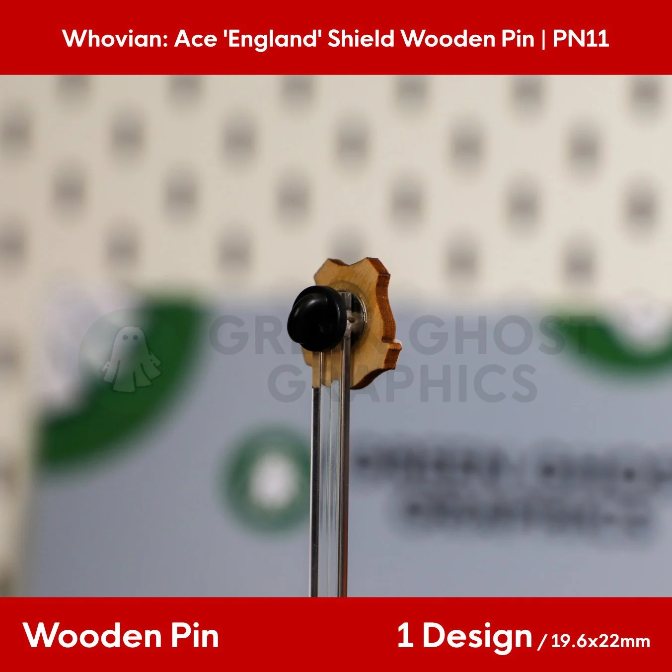 The back of a shield‑shaped wooden pin with a natural wood finish and black rubber clasp displayed on a clear stand.
