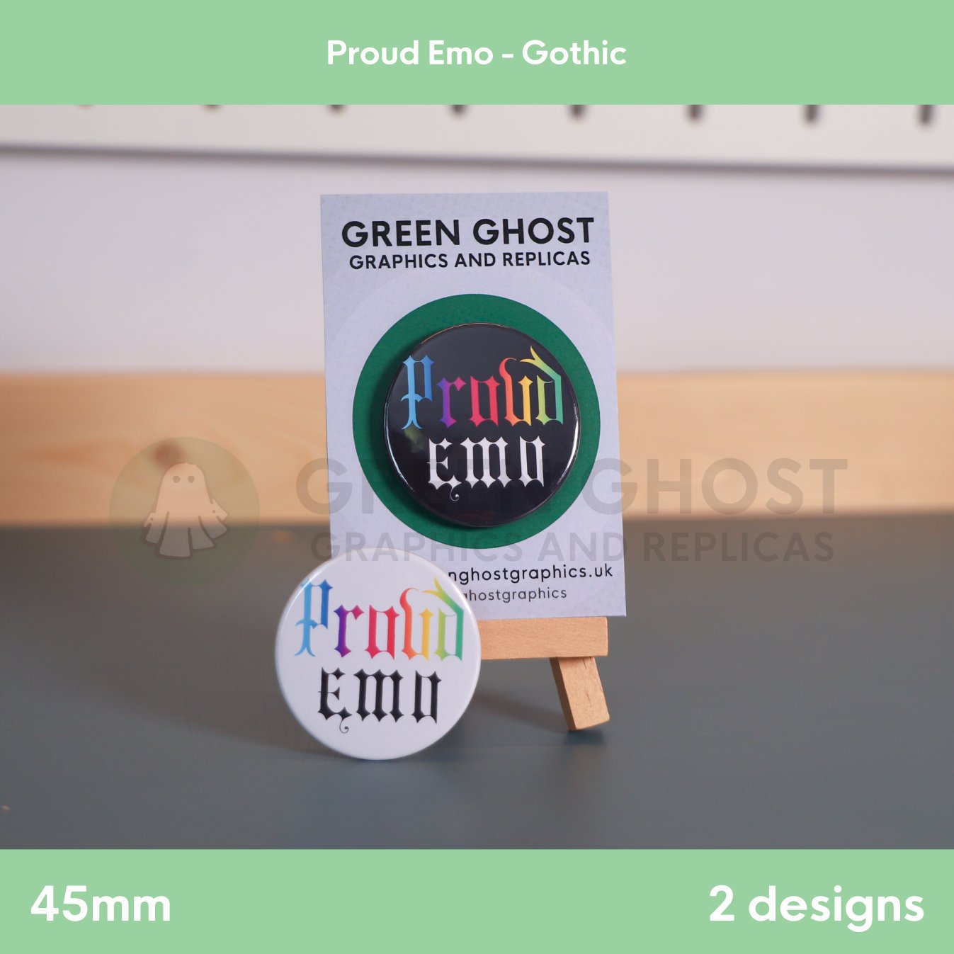 A pair of round badges, one black and one white with rainbow “Proud Emo” text, displayed together on a wooden easel with a branded card behind them.