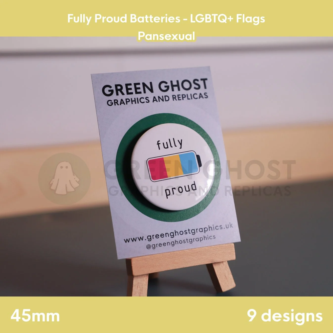 A round badge with a pink, yellow, and blue battery design displayed on a branded backing card on a wooden easel.