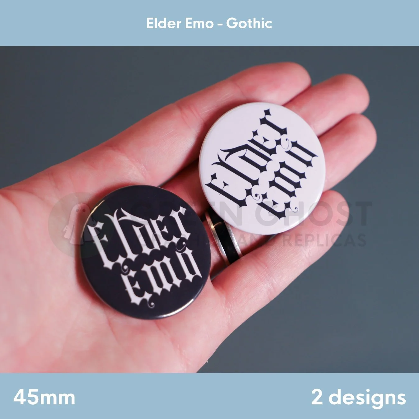 A hand holds two round badges, one black with white Gothic "Elder Emo" text and one white with black Gothic text, against a muted background.