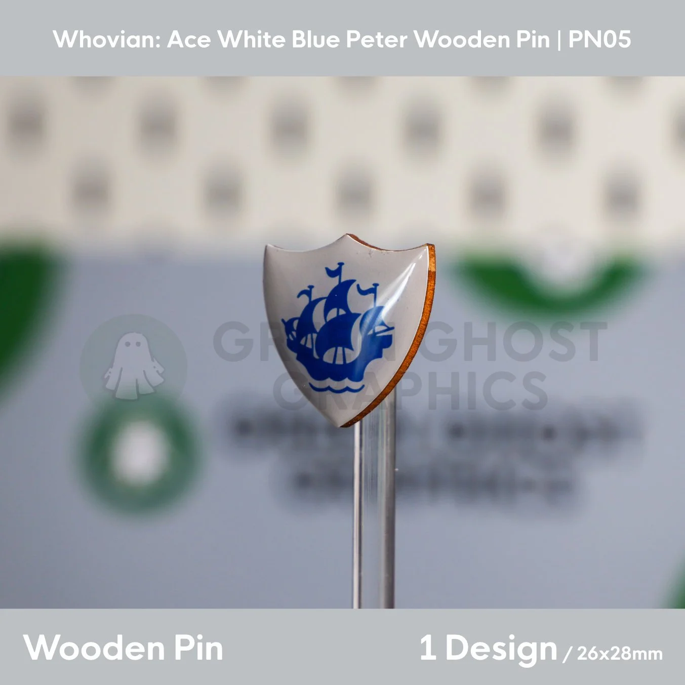 A shield‑shaped wooden pin showing a blue sailing ship on a white background displayed at an angle on a transparent stand.