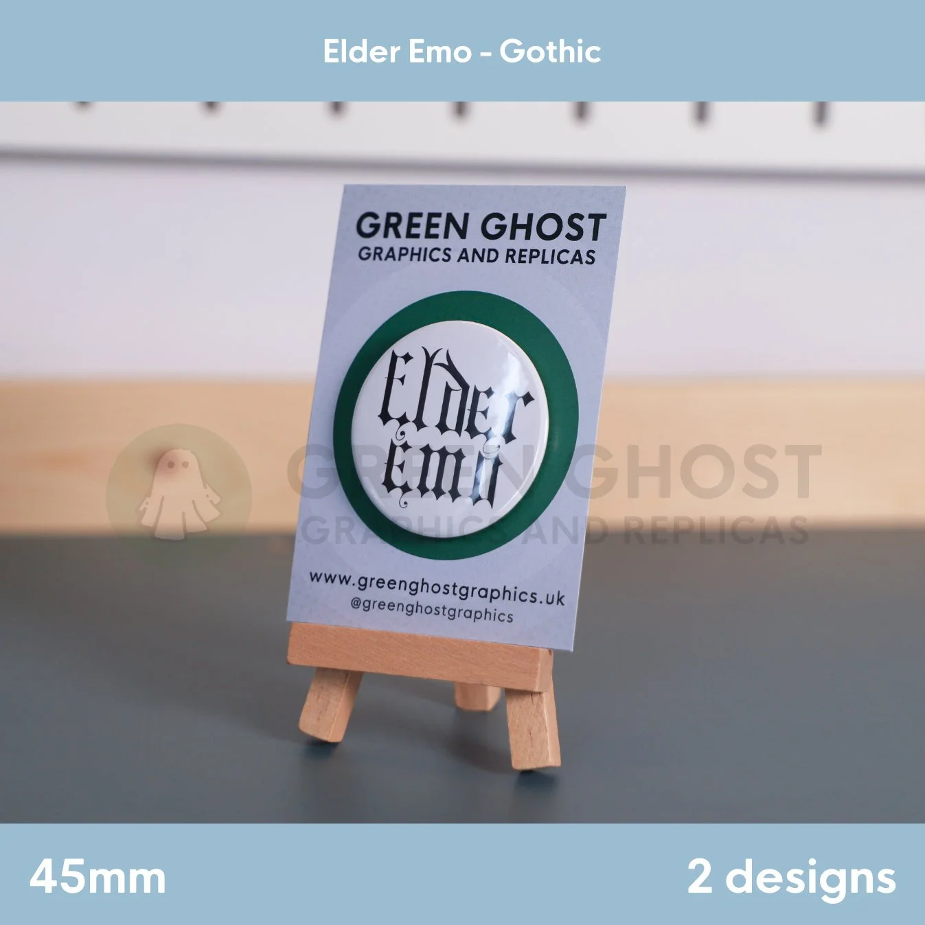 A round white badge with black Gothic "Elder Emo" text shown on a branded card resting on a wooden easel.