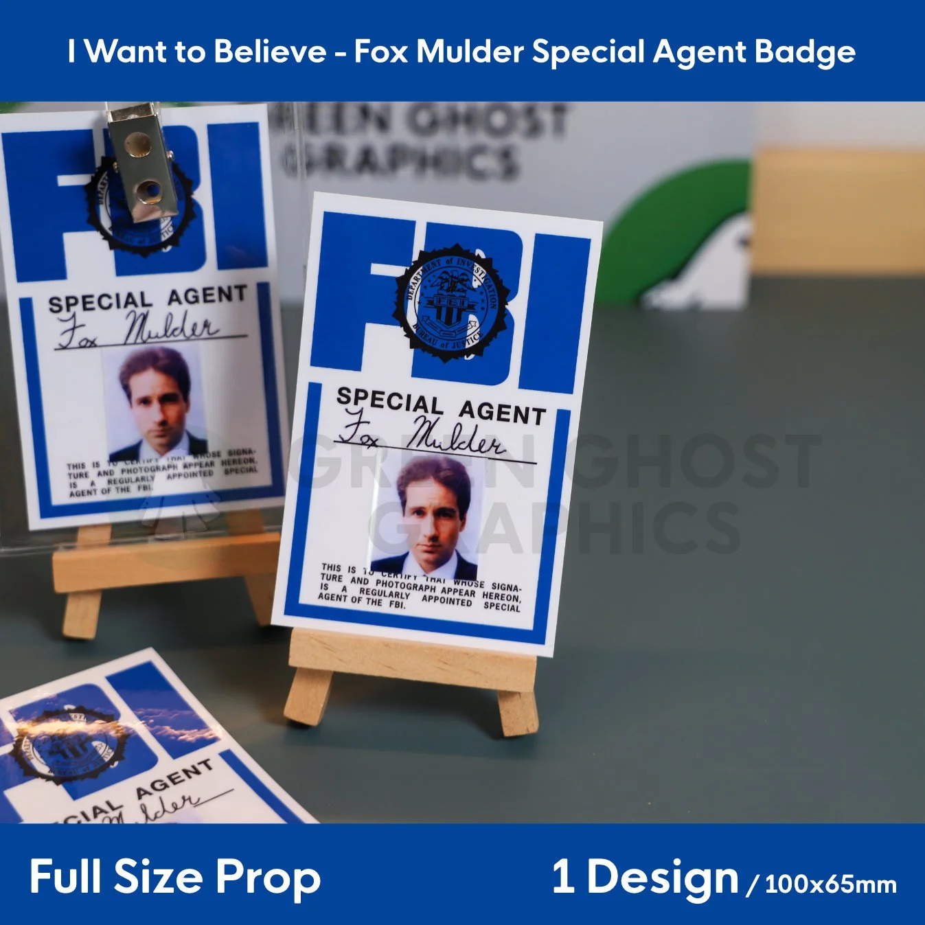 A rectangular blue and white FBI badge with the text “SPECIAL AGENT Fox Mulder” shown upright on a small wooden easel.