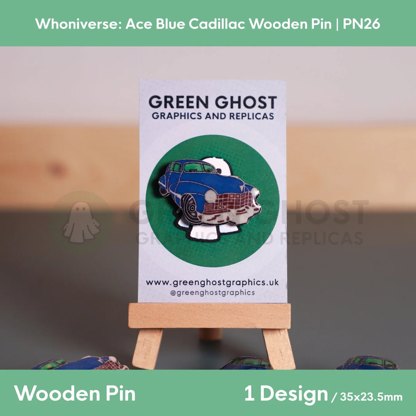 A blue Cadillac wooden pin mounted on a branded backing card on a wooden easel, with multiple identical pins scattered around it on a flat surface.