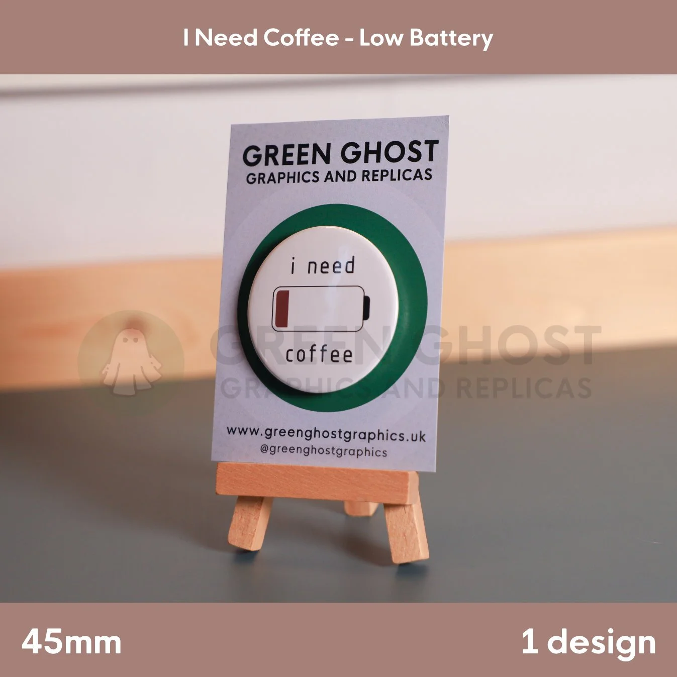 A circular white badge showing a low‑battery symbol and “i need coffee” mounted on a branded card on a wooden easel.