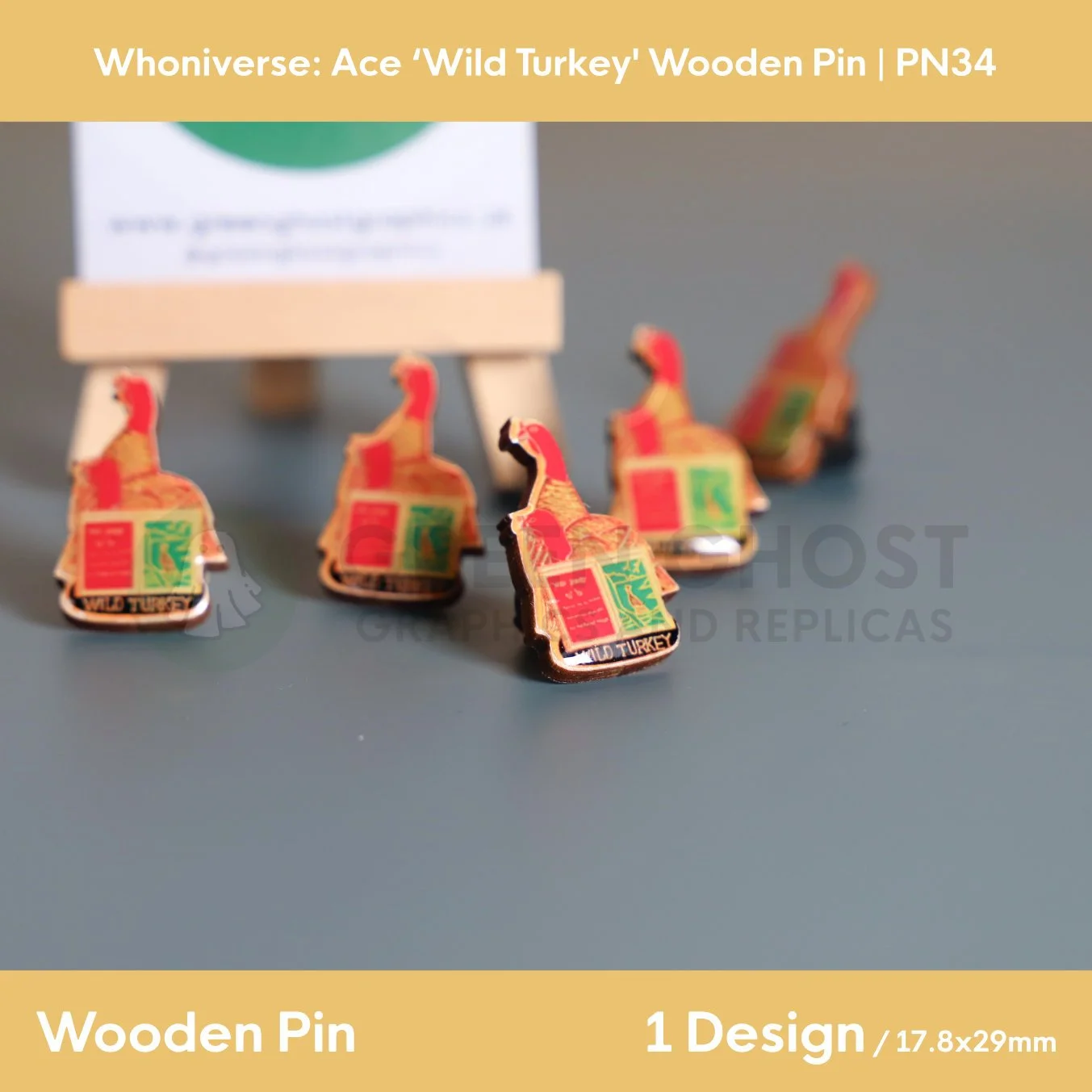 A group of wooden turkey and open book pins displayed on a flat surface, with one pin in sharp focus at the front and others blurred behind it near a wooden easel.