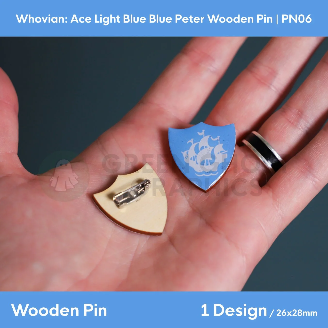 A blue shield‑shaped wooden pin featuring a white sailing ship emblem shown in a hand alongside the natural wood reverse with a metal brooch fastening.