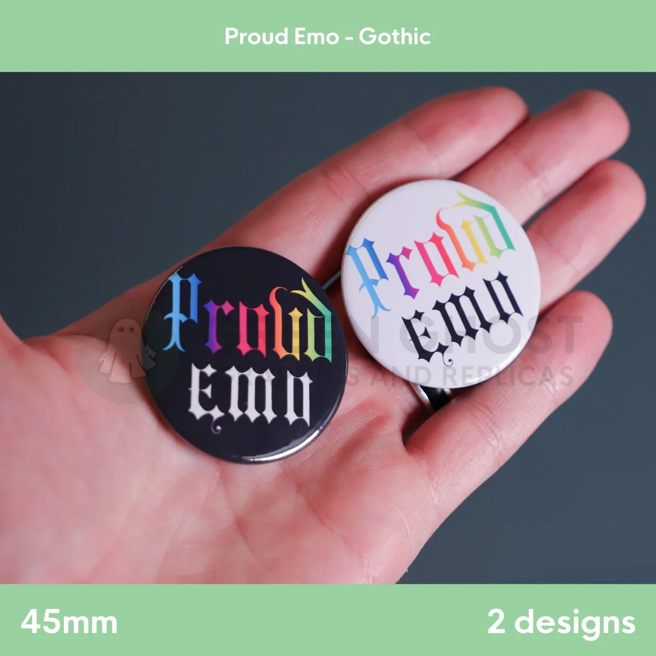 A hand holds two round badges, one black and one white, each featuring rainbow‑coloured “Proud Emo” text against a soft background.