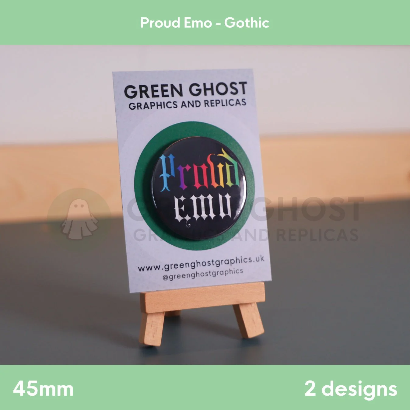 A round black badge with rainbow “Proud Emo” text displayed on a branded backing card on a wooden easel.