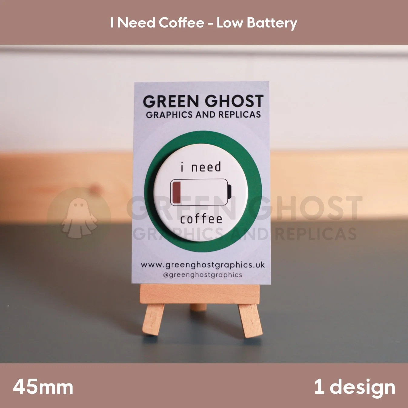 A round badge with a nearly empty battery icon and the words “i need coffee” displayed on a wooden easel with a branded card.