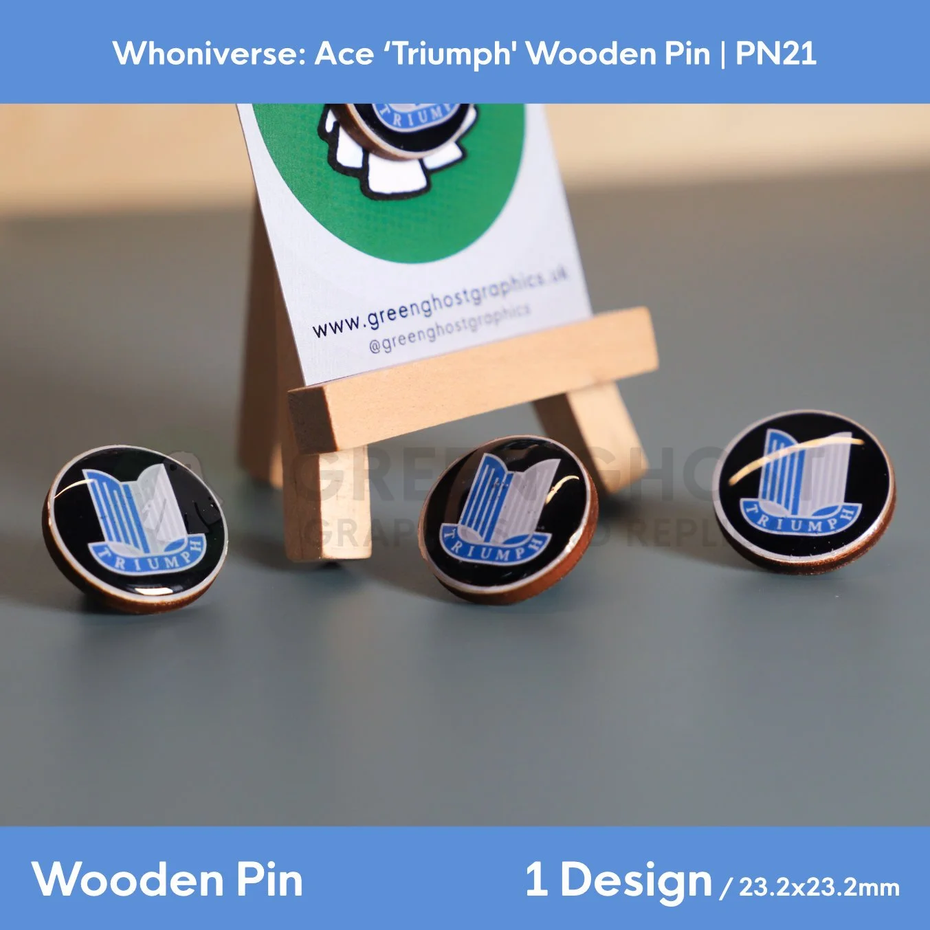 Three circular wooden “TRIUMPH” pins displayed on a flat surface, with one pin propped on a wooden easel holding a branded backing card.