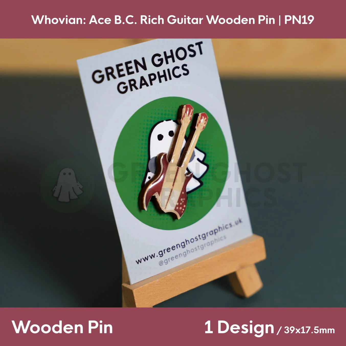 A brown and cream double‑neck guitar‑shaped wooden pin mounted on a Green Ghost Graphics display card on a small wooden easel.