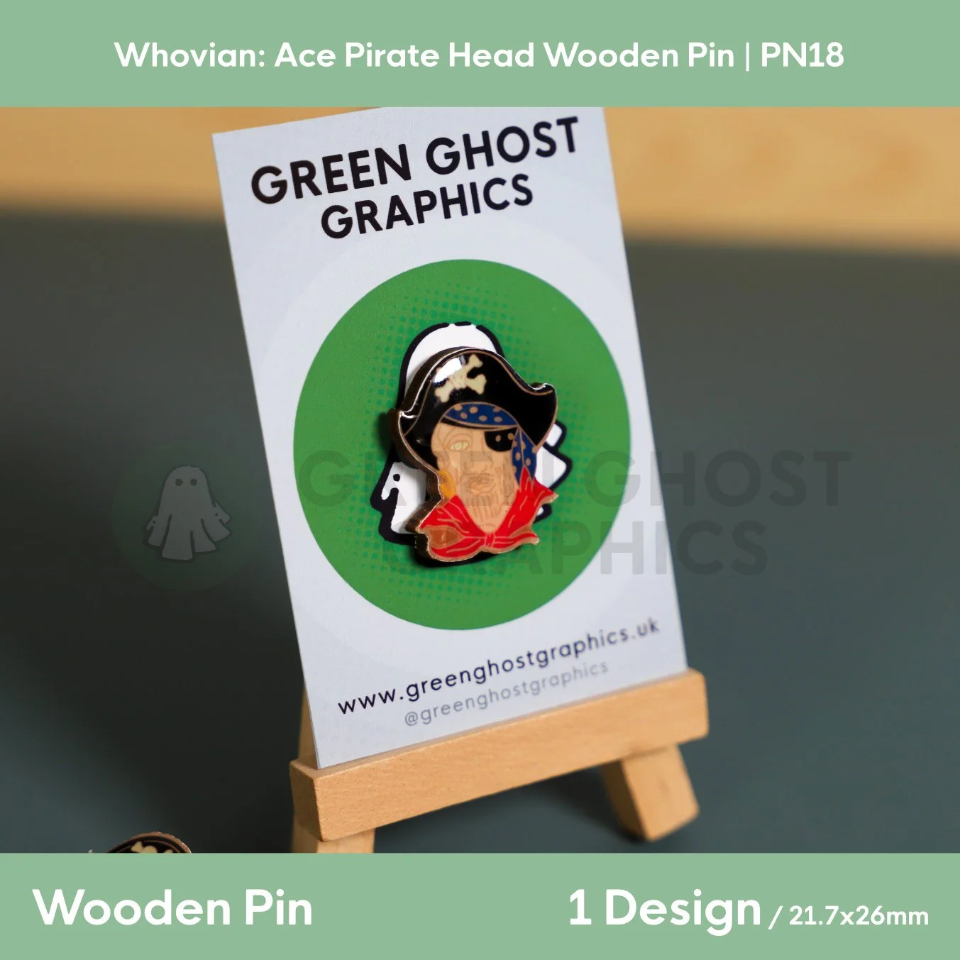 A pirate‑head‑shaped wooden pin with a black hat, blue bandana, eye patch, and red coat mounted on a Green Ghost Graphics display card on a wooden easel.
