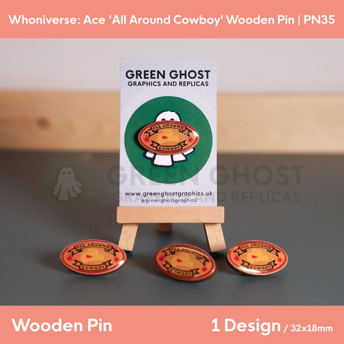 An oval wooden pin with a sandy background and a coloured cowboy hat and text, “ALL AROUND COWBOY” displayed on a branded backing card on a wooden easel with several identical pins arranged in front.