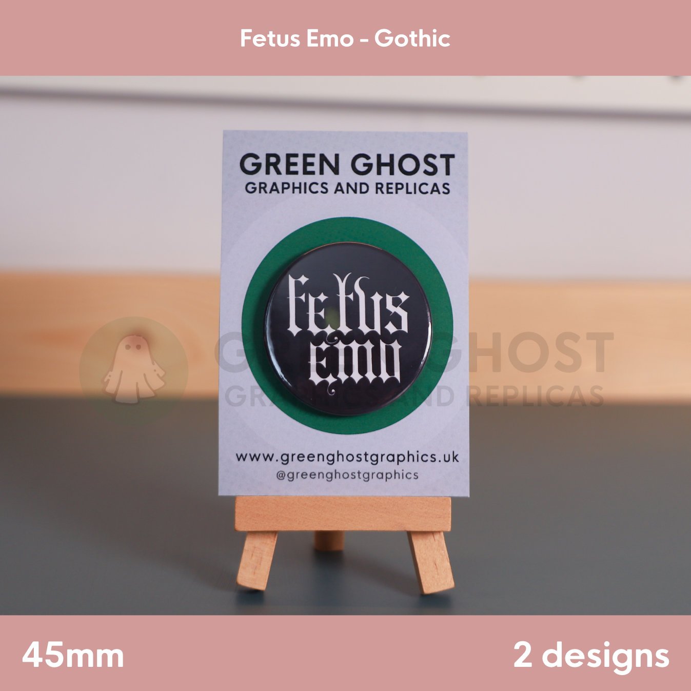 A round black badge with white Gothic text "Fetus Emo" shown on a branded card resting on a wooden easel.