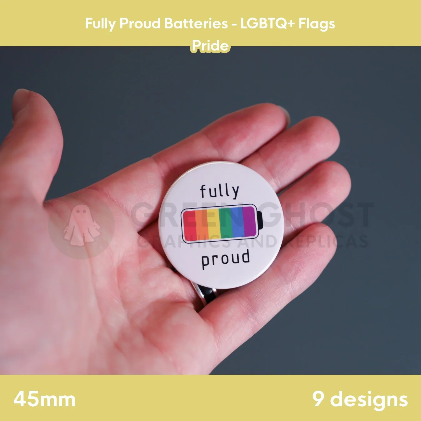 A round badge with a rainbow battery design held in a hand against a grey background.