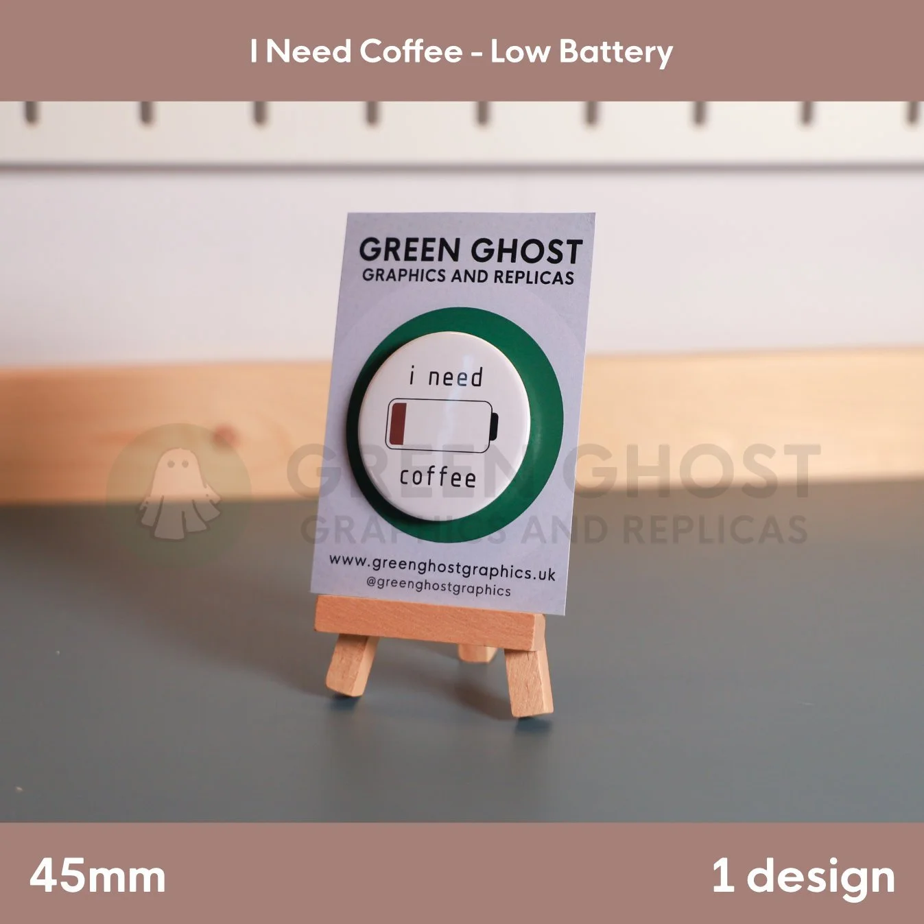 A circular white badge and “i need coffee” text beside a low‑battery icon mounted on a branded backing card.