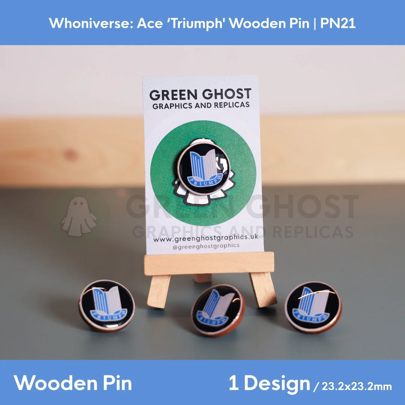 A circular wooden pin with a blue and white emblem and the word “TRIUMPH,” displayed on a branded backing card on a wooden easel, with additional identical pins arranged around it.