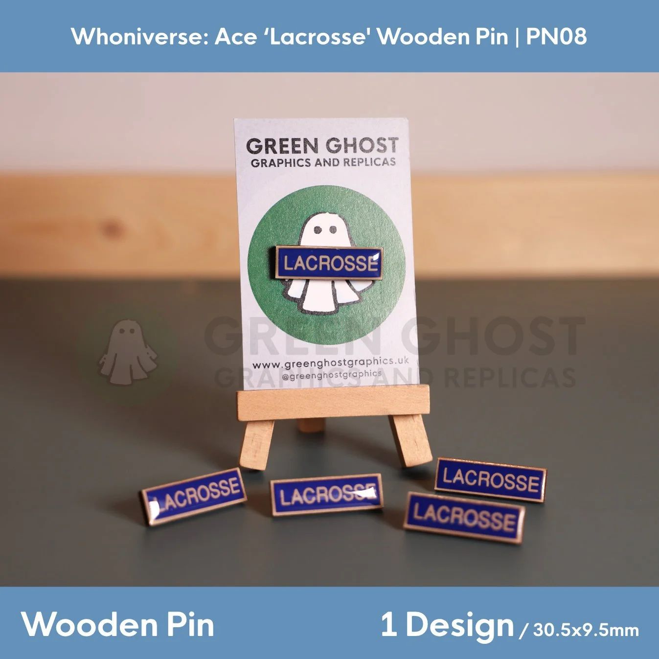 A rectangular wooden pin with a blue background and the word “LACROSSE” in white letters, displayed on a branded backing card on a wooden easel with additional identical pins arranged around it.