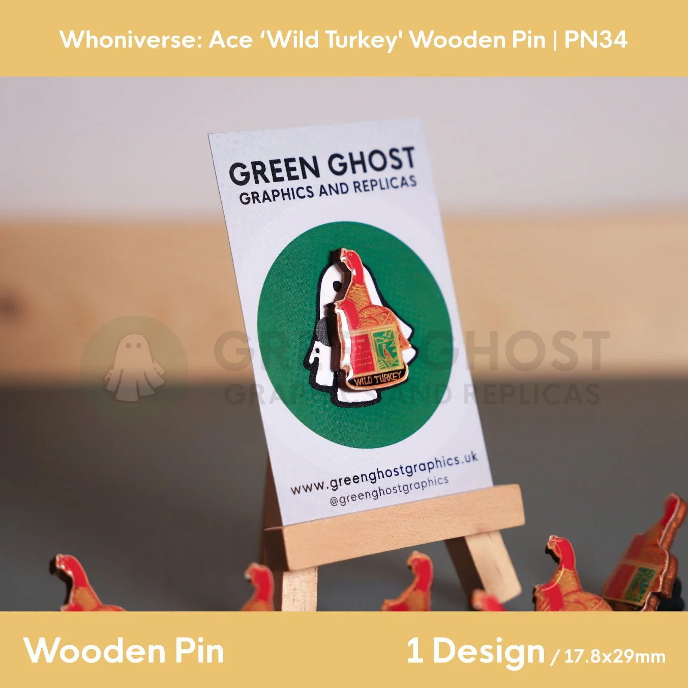 A red and golden turkey and open book wooden pin attached to a branded backing card on a wooden easel, with several identical pins arranged neatly in front.