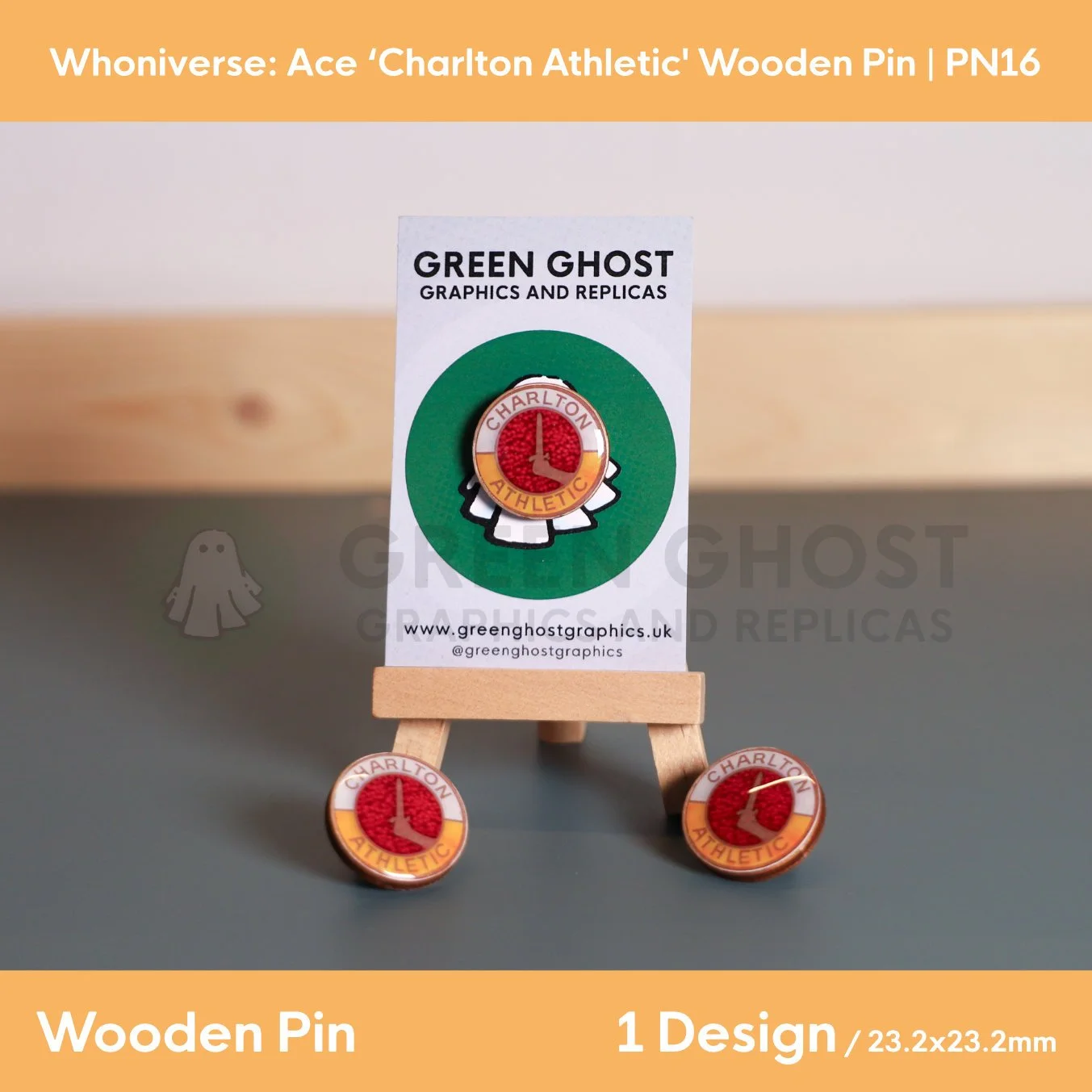 A circular wooden pin featuring a red centre with a white sword emblem and the text “CHARLTON ATHLETIC,” displayed on a branded backing card on a wooden easel with two identical pins placed beside it.