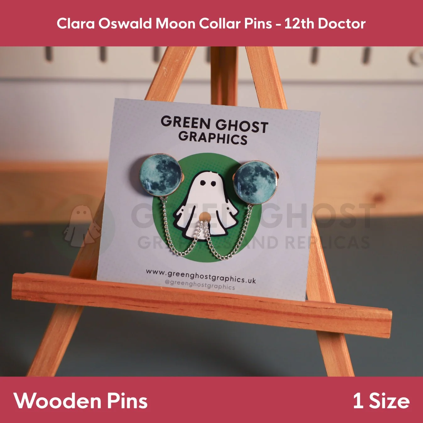 A pair of moon‑design wooden pins joined by a chain and presented on a branded display card set on a wooden easel.