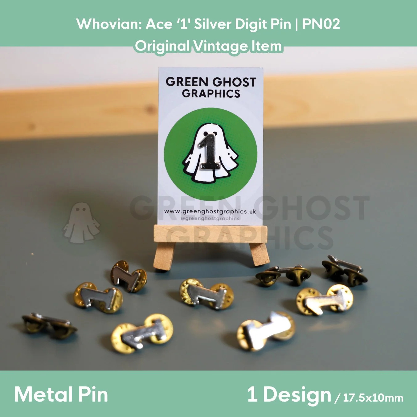 Several silver number “1” metal pins arranged on a tabletop around a Green Ghost Graphics display card mounted on a wooden easel.