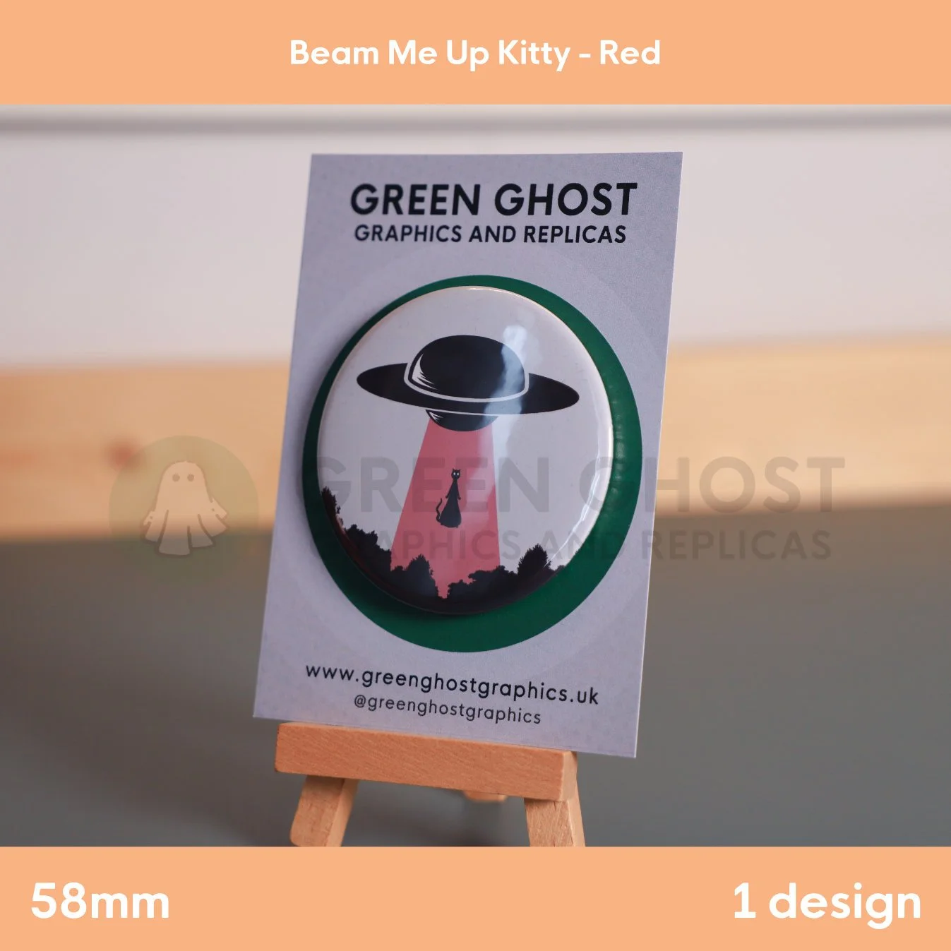 A round badge with a red UFO beam lifting a cat displayed on a branded backing card on a wooden easel.