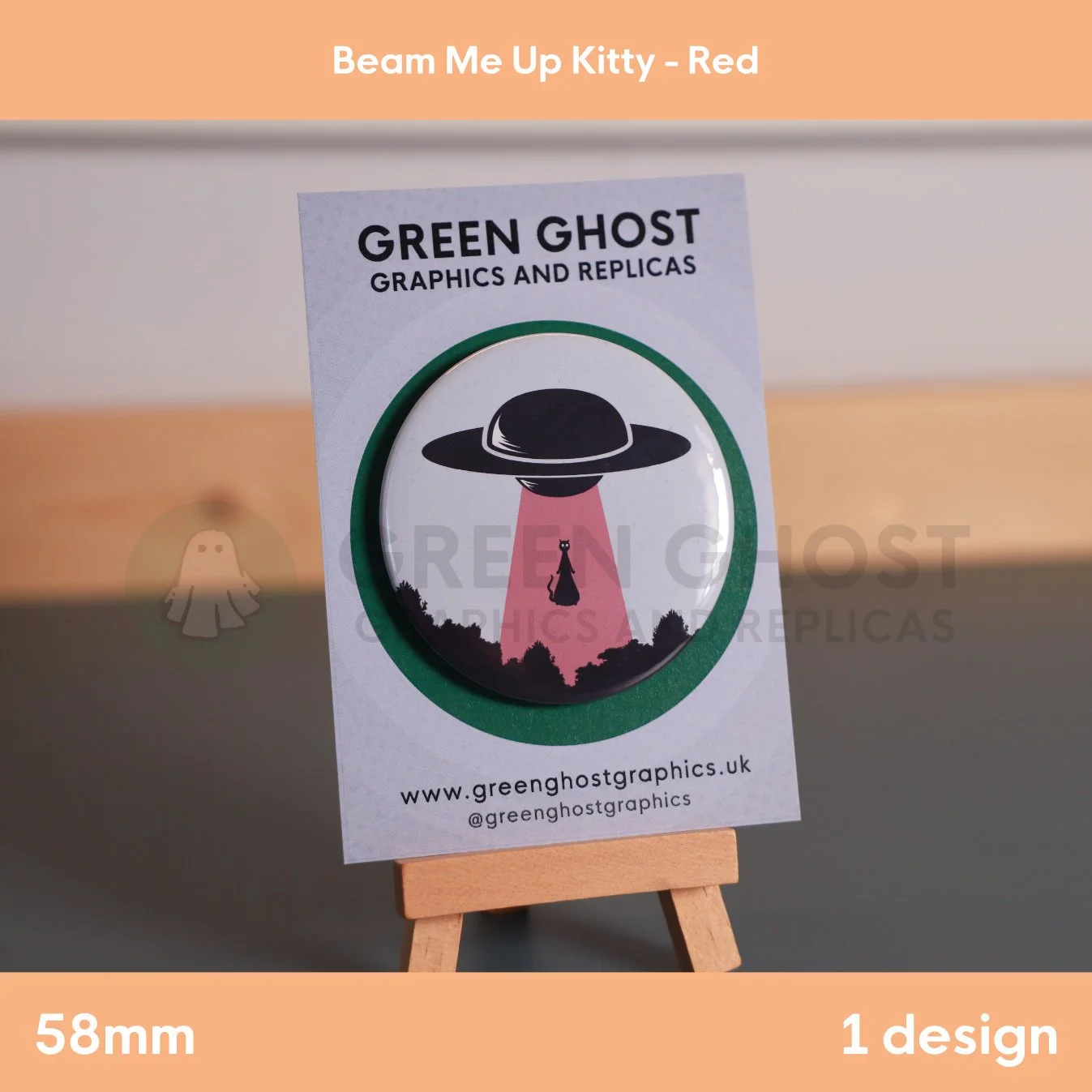 A round badge with a red UFO beam lifting a cat displayed on a branded backing card on a wooden easel.