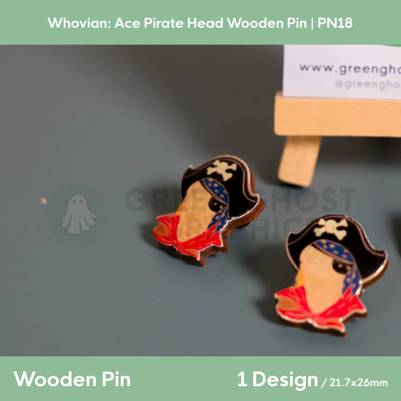 Two pirate‑head‑shaped wooden pins with black hats, blue bandanas, and red collars displayed on a dark surface beside a wooden easel.