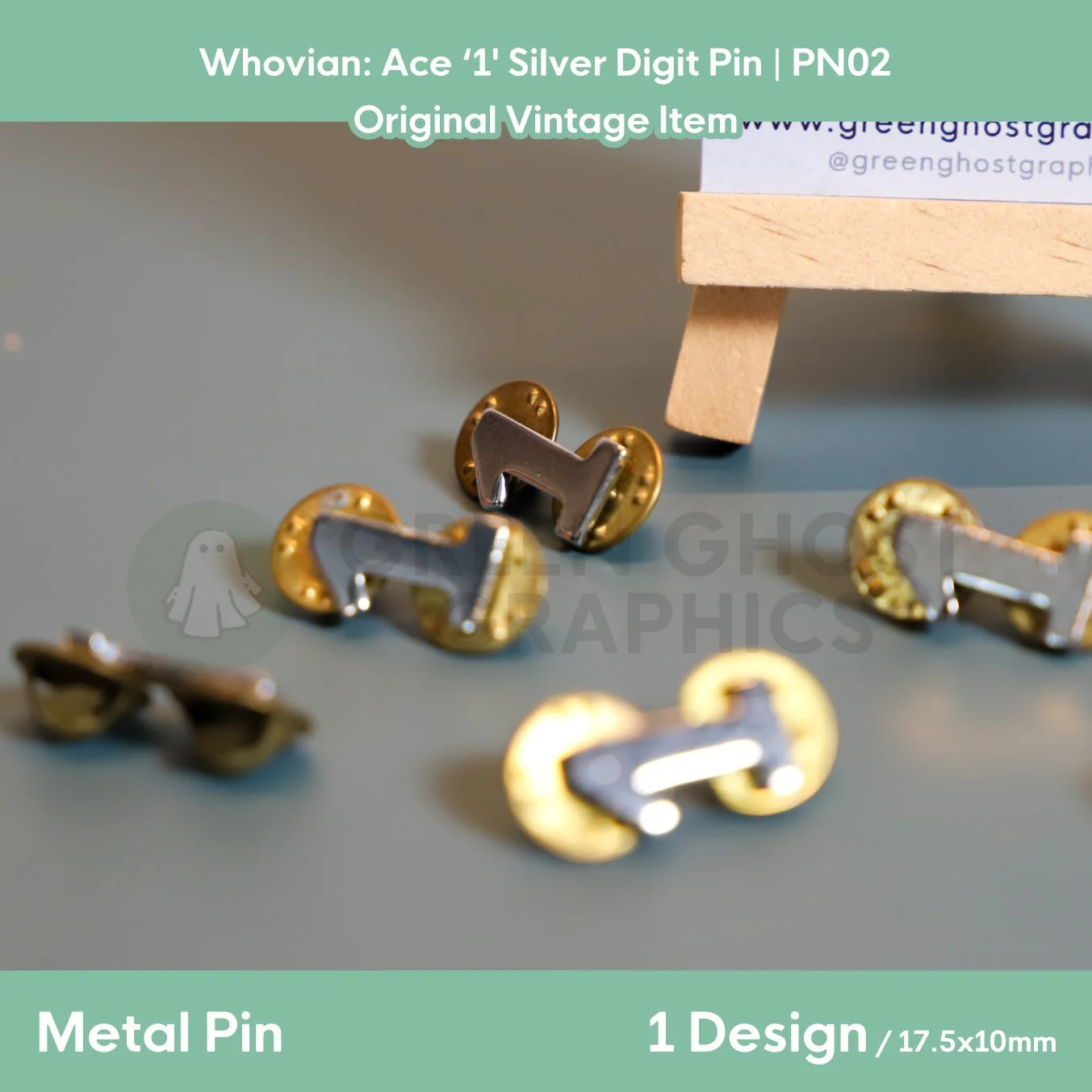 Several silver number “1” pins with gold butterfly clasps arranged on a tabletop in front of a display stand.