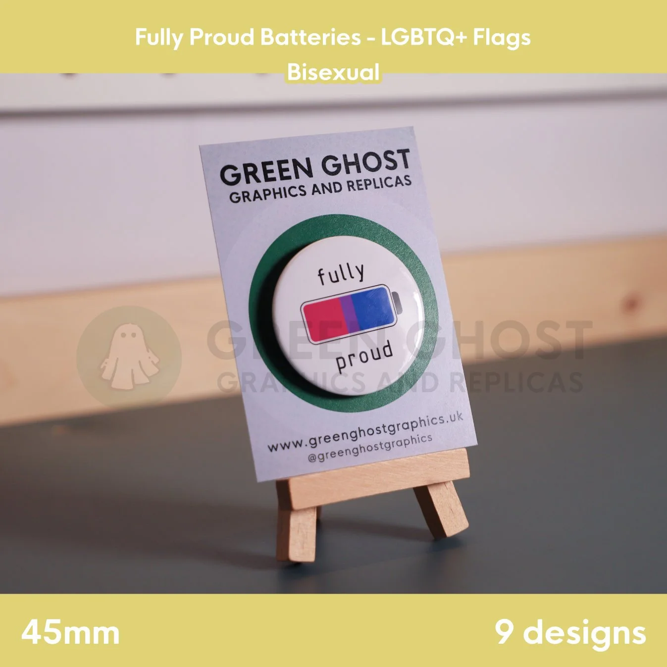 A round badge with a pink, purple, and blue battery design displayed on a branded backing card on a wooden easel.