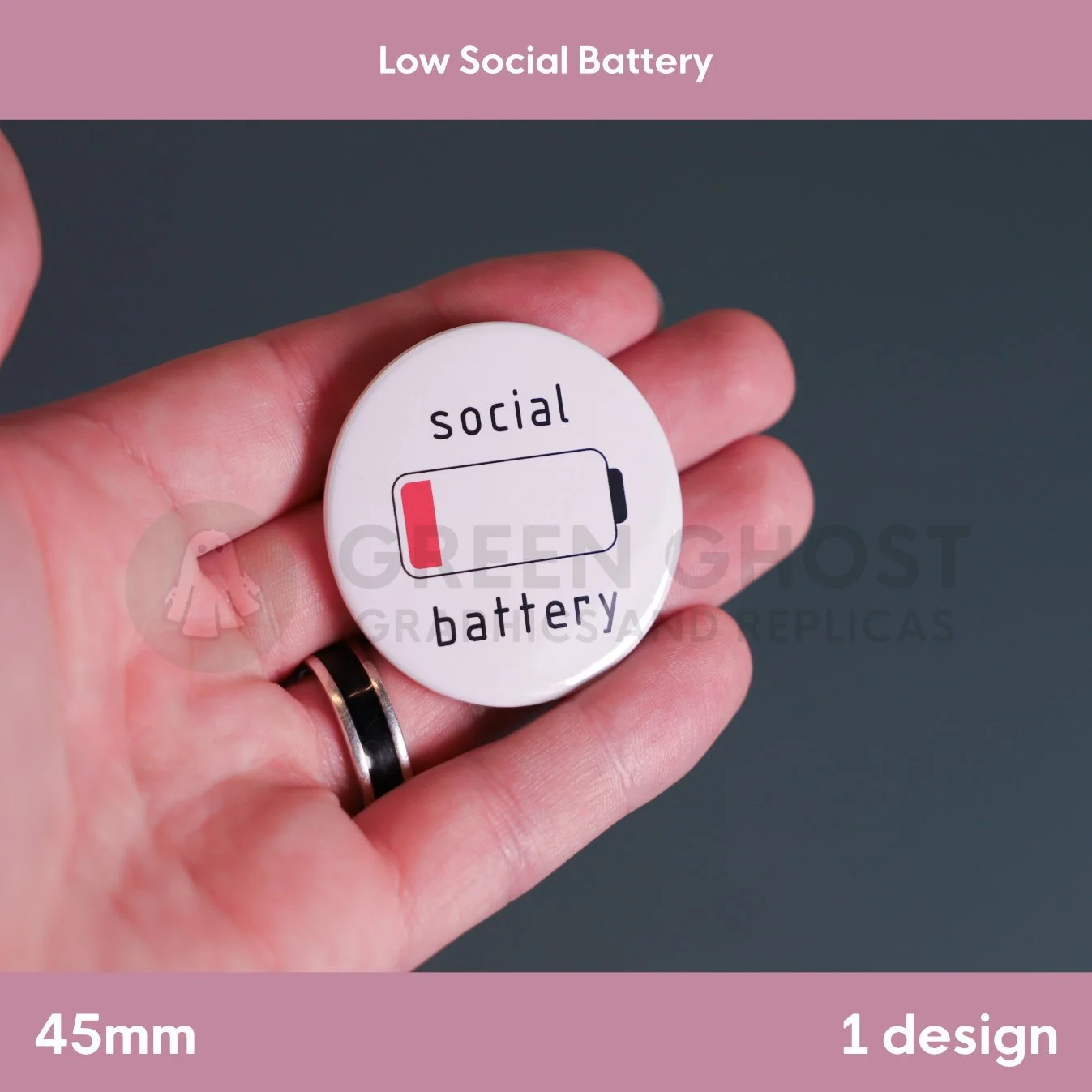 A round white badge with a red low‑battery icon and the phrase “social battery” held in a hand against a muted background.
