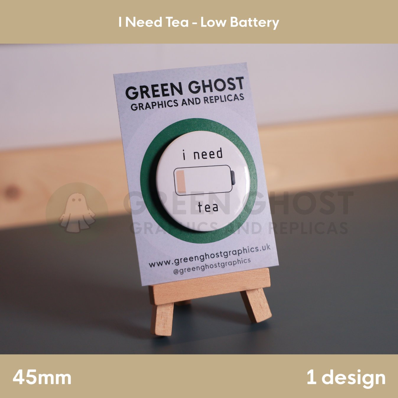 A circular white badge showing a low‑battery symbol and “i need tea” mounted on a branded card on a wooden easel.