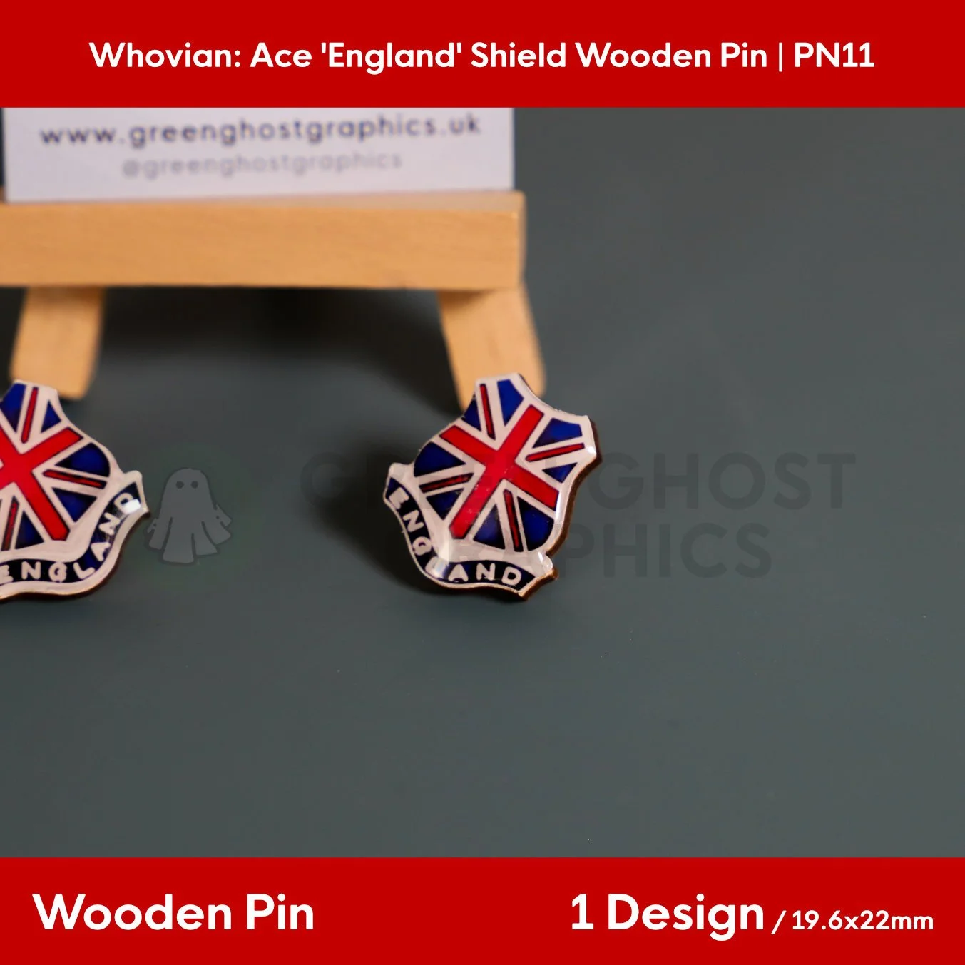 A red, white, and blue shield‑shaped wooden pin showing the text “ENGLAND” positioned on a dark surface in front of a wooden easel