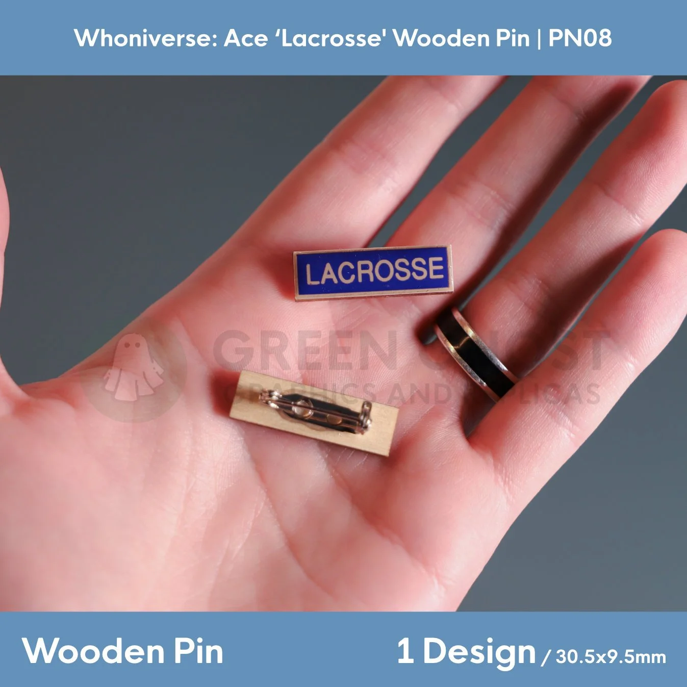 A close‑up view of the wooden “LACROSSE” pin showing the front design with white lettering on blue and the back with a metal clasp, held in a hand.