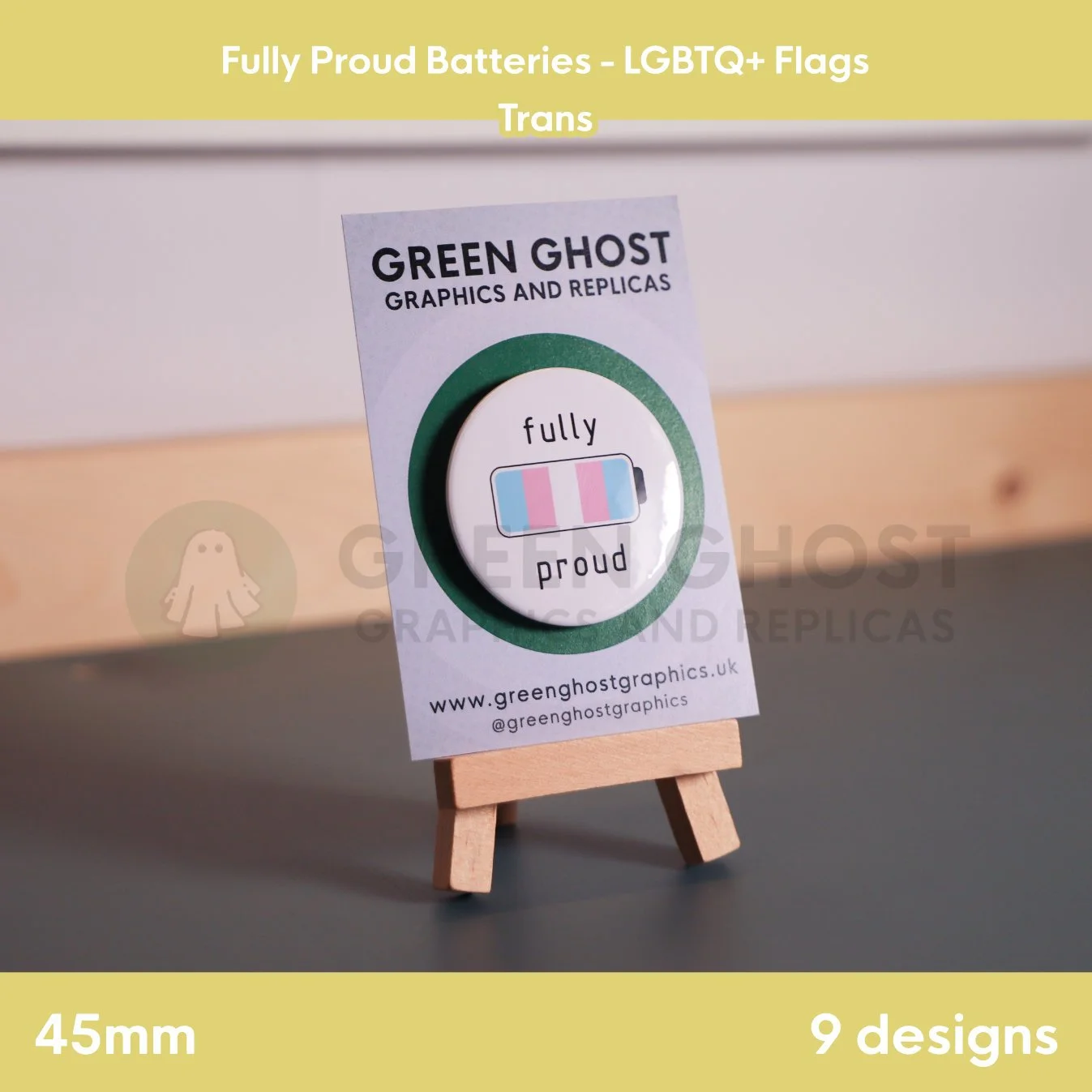 A round badge with a light blue, pink, and white battery design displayed on a branded backing card on a wooden easel.