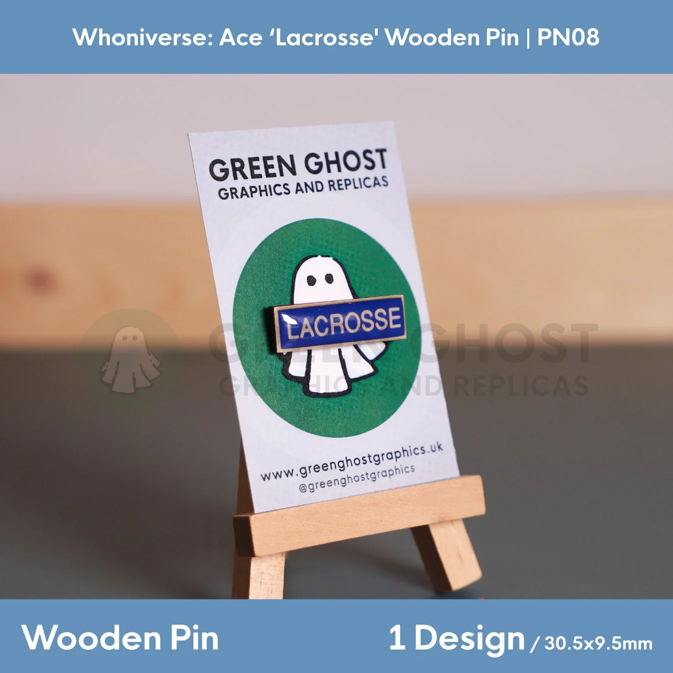 A rectangular wooden “LACROSSE” pin on a branded backing card with a ghost illustration, displayed on a wooden easel with product details shown below.