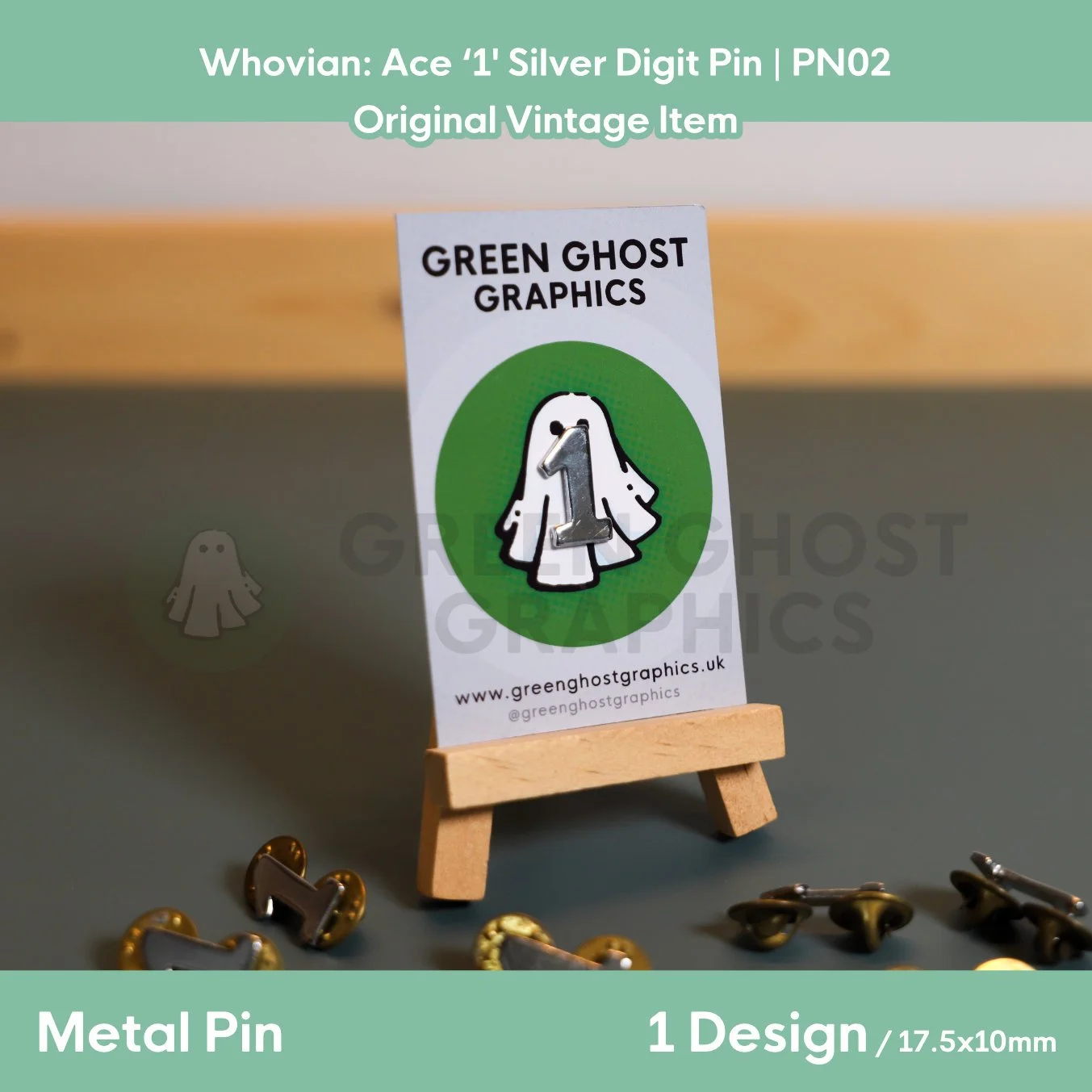 A metallic digit “1” pin attached to a Green Ghost Graphics card with a white ghost illustration and green circular background, shown on an easel.
