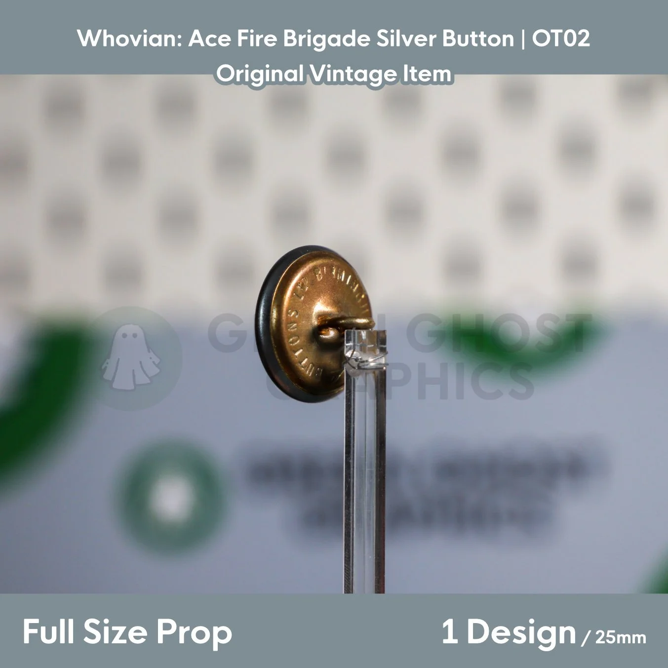 The reverse of a round brass‑coloured button with maker’s text around the edge displayed on a clear stand.