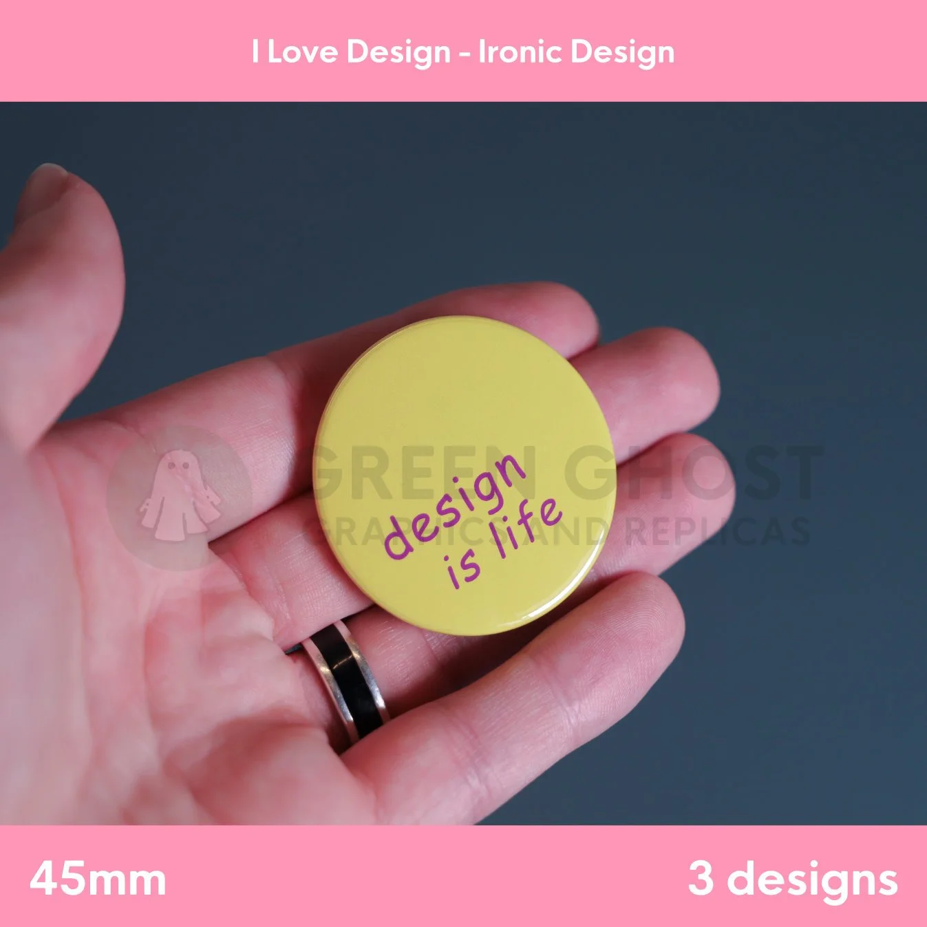 A round yellow badge with purple “design is life” text held in a hand against a dark grey background.