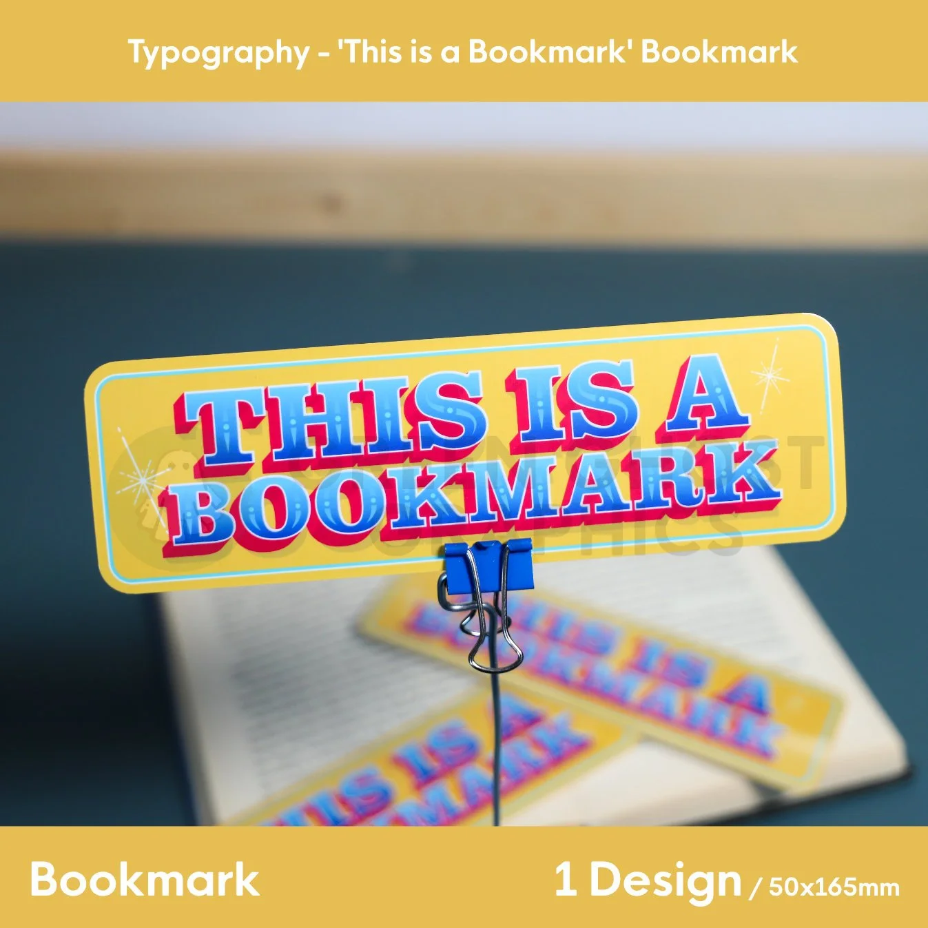 A rectangular yellow bookmark with bold blue‑and‑red “THIS IS A BOOKMARK” text resting across the pages of an open book.