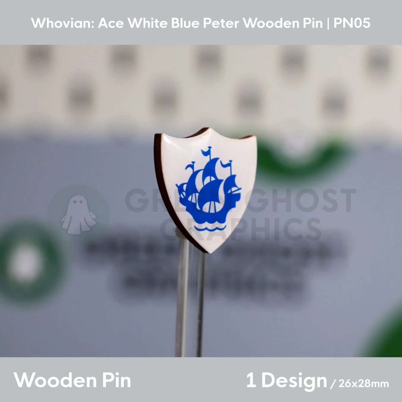 A white shield‑shaped wooden pin with a blue ship emblem presented upright on a clear display rod against a blurred background.