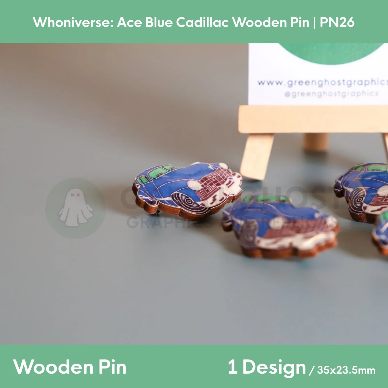 Several wooden pins shaped like blue Cadillac cars arranged on a smooth grey surface, with a wooden easel holding a branded backing card in the background.