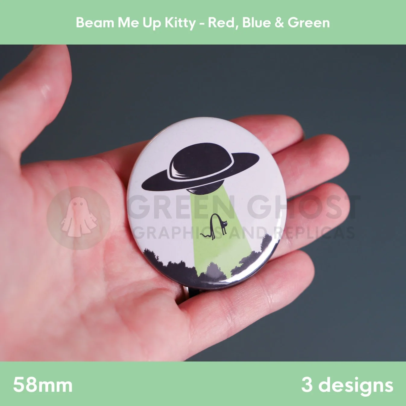 A round badge with a green UFO beam lifting a cat, held in a hand against a grey background.