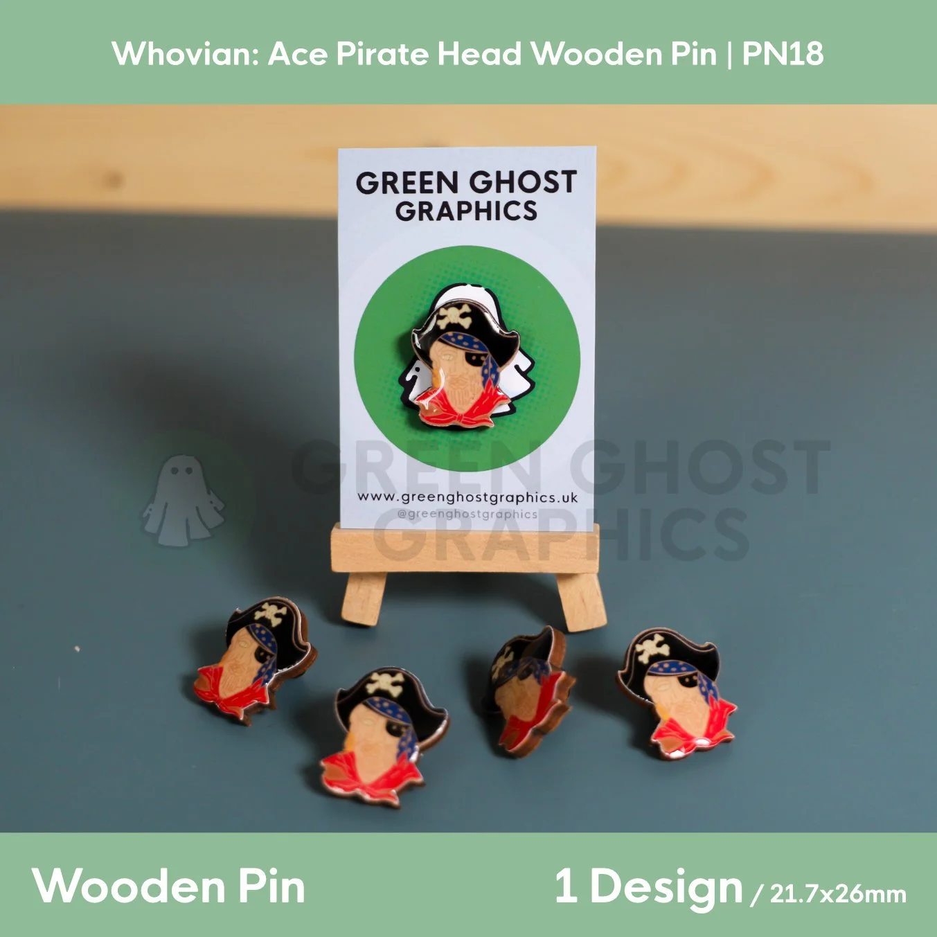 Four pirate‑head wooden pins featuring eye patches, skull‑and‑crossbones hats, and red clothing arranged around a Green Ghost Graphics display card on a small easel.